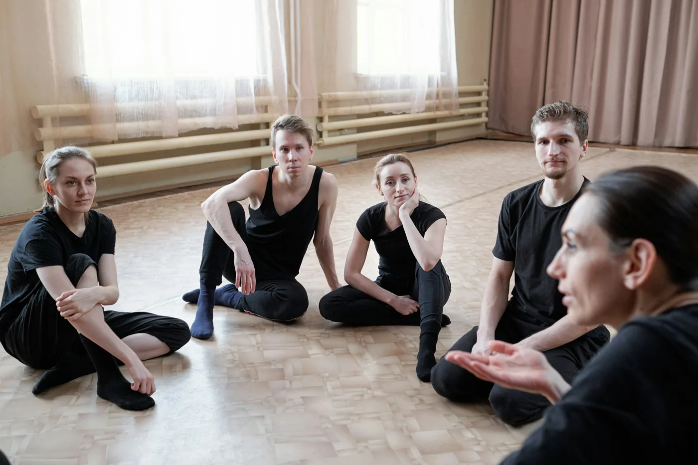 People seated in a floor circle in a rehearsal studio.