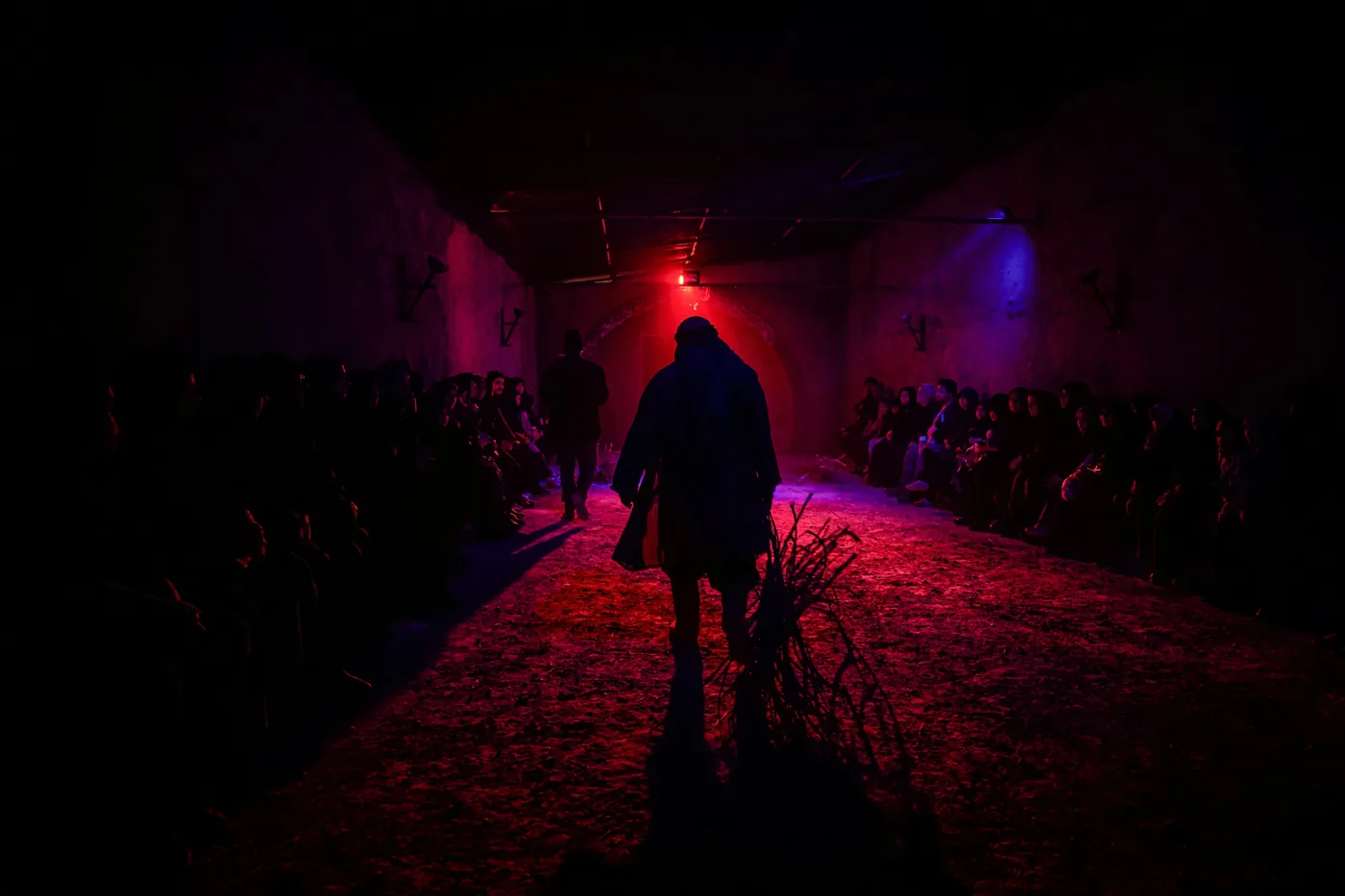 Red-lit stage with a central figure and seated audience.