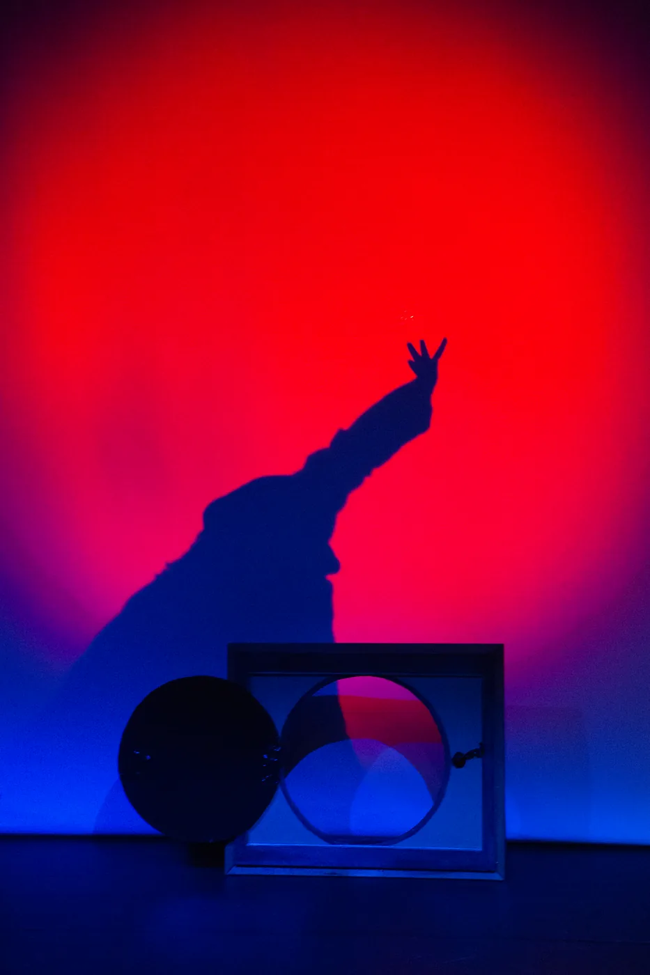 A raised hand casts a shadow against a red and blue stage backdrop.