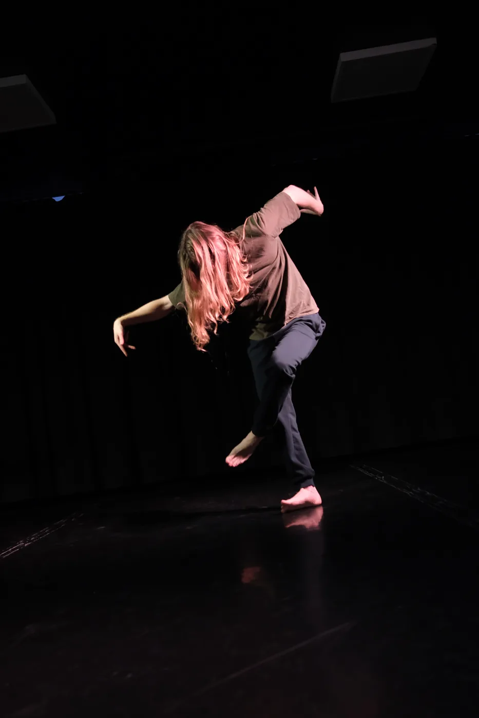 A solo dancer balances on one foot under a spotlight.