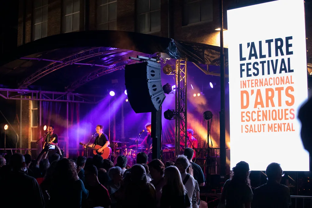Musicians perform beneath purple stage lights beside a large festival sign.