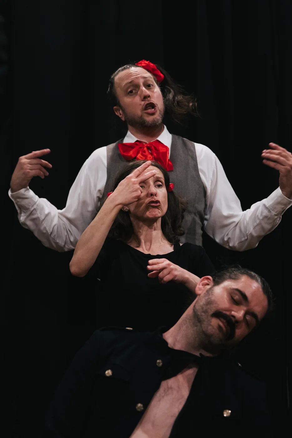 Three performers in contrasting costumes act on a dark stage.