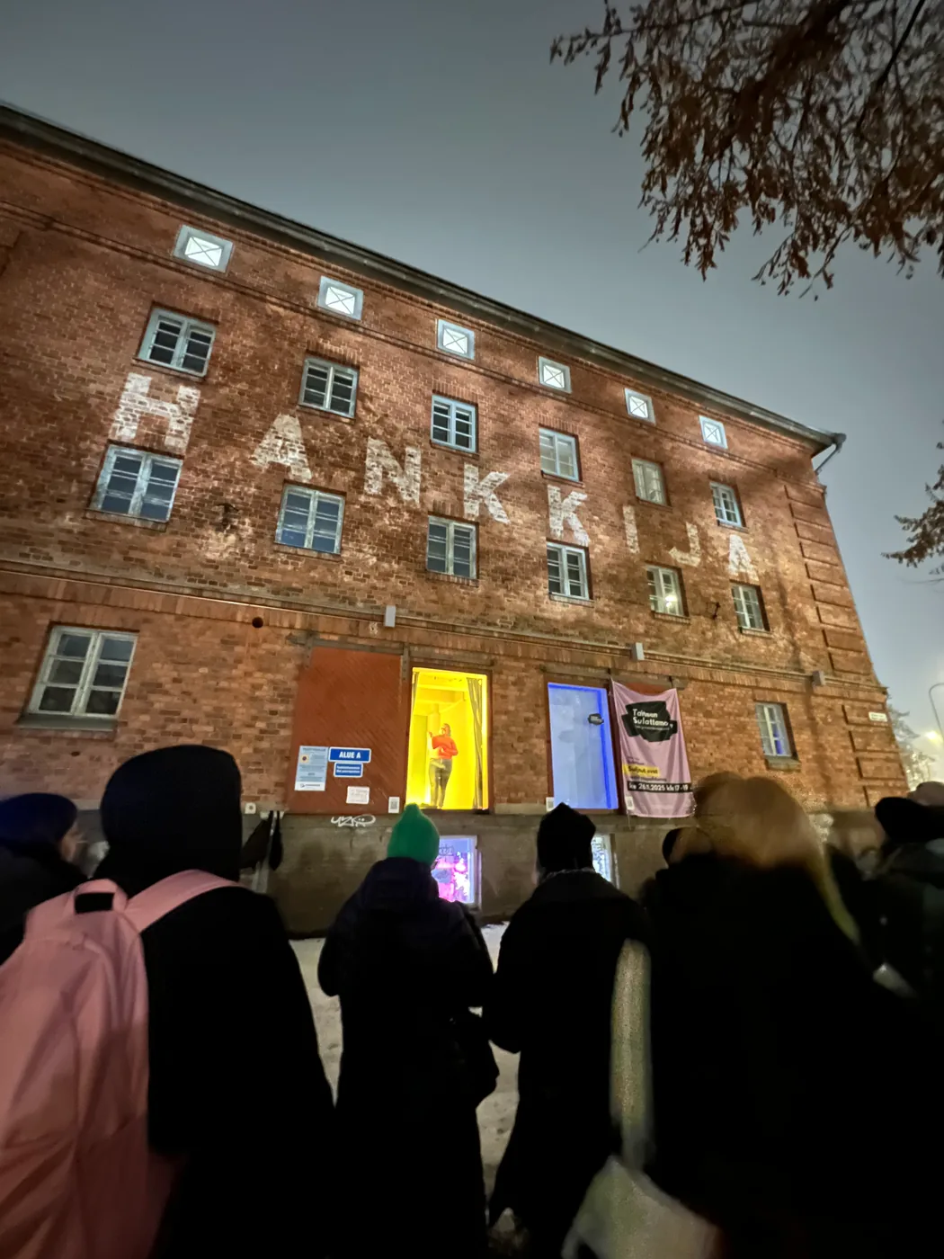 A brick building with illuminated entrances and event banners at dusk.